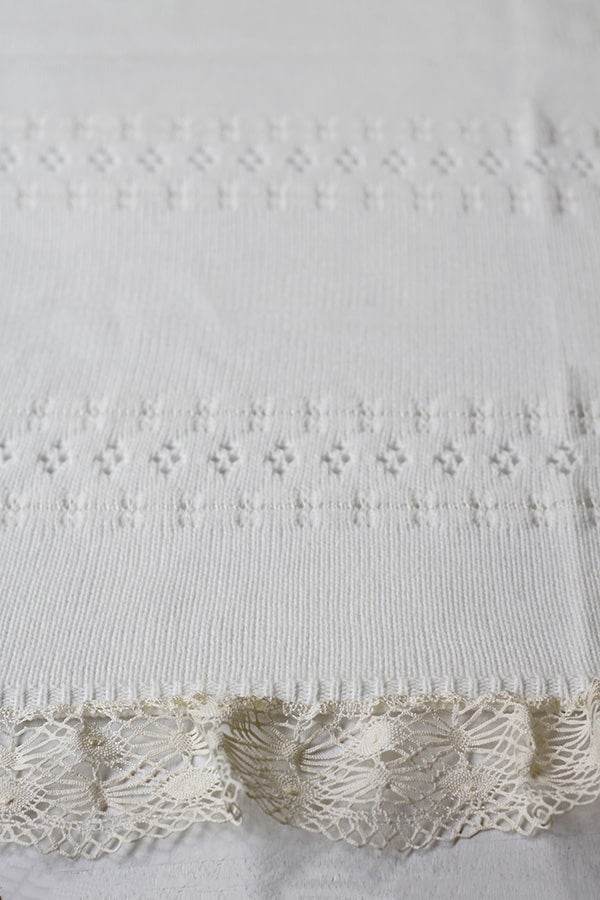 Couverture bébé pour cérémonie ou baptême en lainage blanc cassé, avec motifs ajourés et large galon de dentelle. Gros plan sur dentelle.