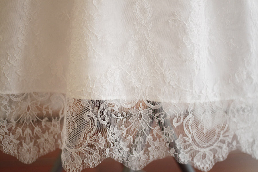 Robe de baptême traditionnelle bébé en dentelle fine de couleur blanc cassé. Corsage manches longues. Cousu main en France. Gros plan bordure dentelle.