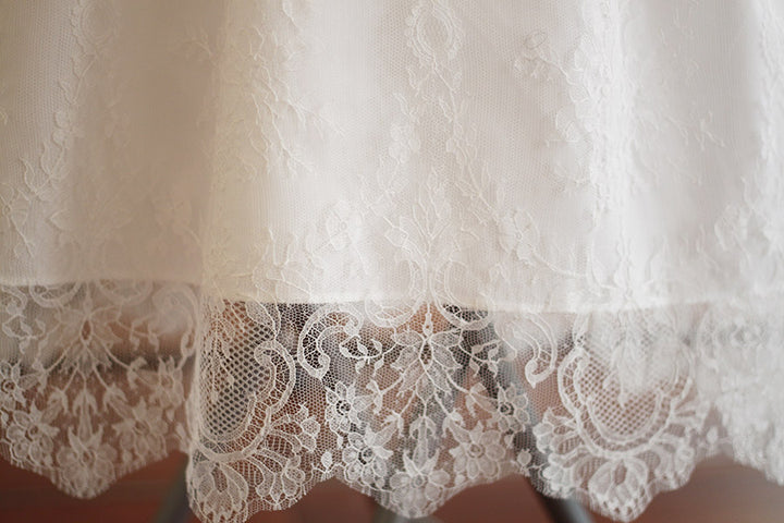 Robe de baptême traditionnelle bébé en dentelle fine de couleur blanc cassé. Corsage manches longues. Cousu main en France. Gros plan bordure dentelle.