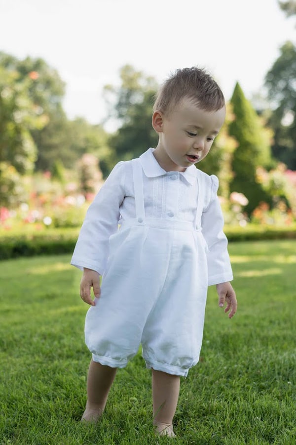 Ensemble baptême bébé garçon Alexandre avec chemise et salopette en lin blanc et dentelle de coton. Création française Fil de Légende. Photo de l'ensemble porté par un petit garçon qui marche.