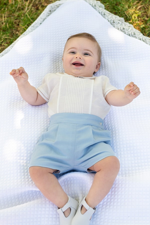Ensemble cérémonie bébé garçon avec chemise de cérémonie manches courtes blanches et short bleu ciel. Modèle Clément, Fil de Légende. Photo de l'ensemble cérémonie bébé porté par un bébé garçon allongé.