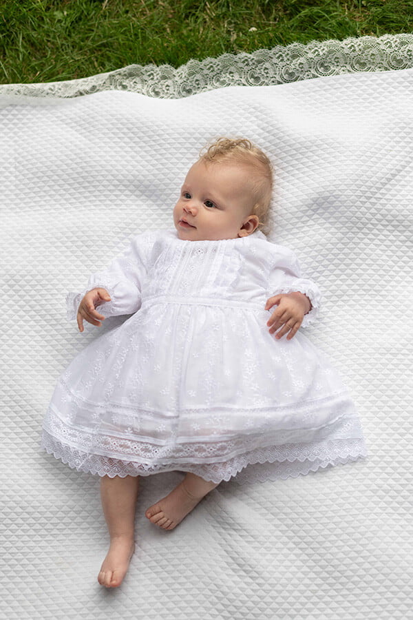 Robe de baptême et de cérémonie pour bébé fille, en broderie anglaise blanche et dentelle de Calais. Robe de baptême haut de gamme, création française Fil de Légende. Photo de la robe portée par un bébé.
