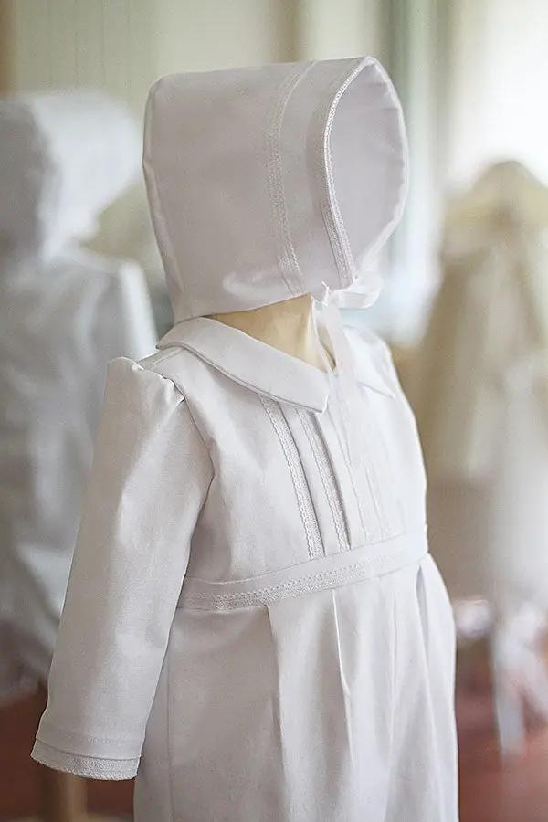 Barboteuse baptême bébé garçon Léo en coton blanc et dentelle de coton. Création française Fil de Légende. Photo de la barboteuse portée avec le bonnet de baptême assorti.