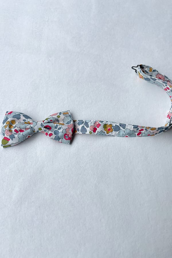 Nœud papillon pour petit garçon en coton Liberty avec fleurs de couleurs bleu gris, rouge et rose. idéal à porter pour un cortège de mariage. Photo du nœud à plat.