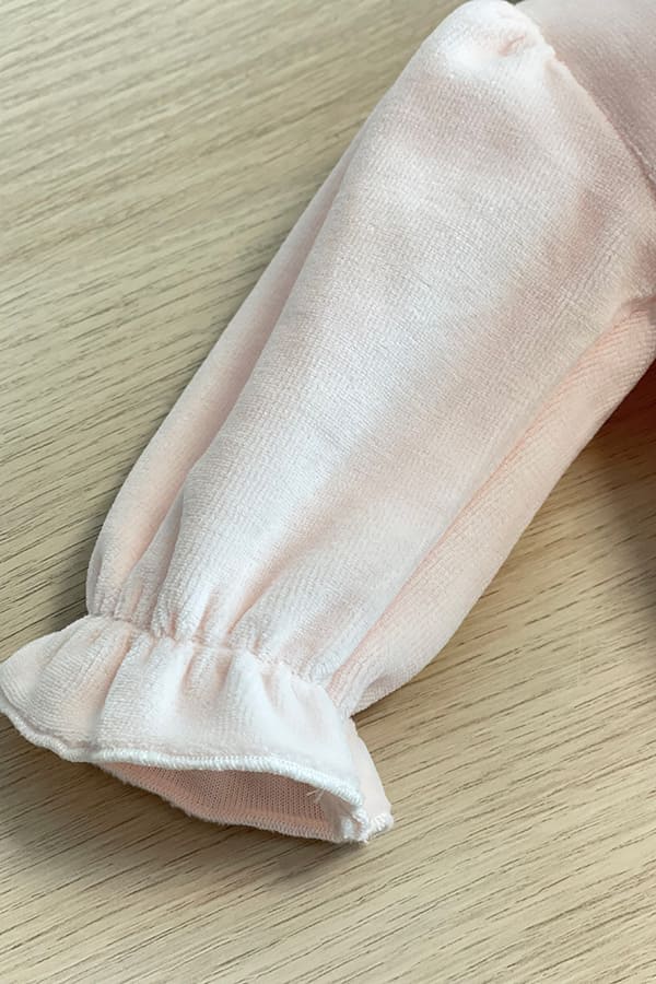 Gros plan sur la manche bouffante du pyjama bébé fille Eva en velours de coton rose pâle, avec poignet resserré par un élastique et terminé par un délicat volant – Fil de Légende.