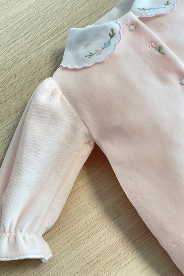 Détail du pyjama bébé fille Eva en velours de coton rose pâle, avec manche bouffante terminée par un volant élastiqué et col blanc festonné brodé de petites fleurs roses et bleues – Fil de Légende.