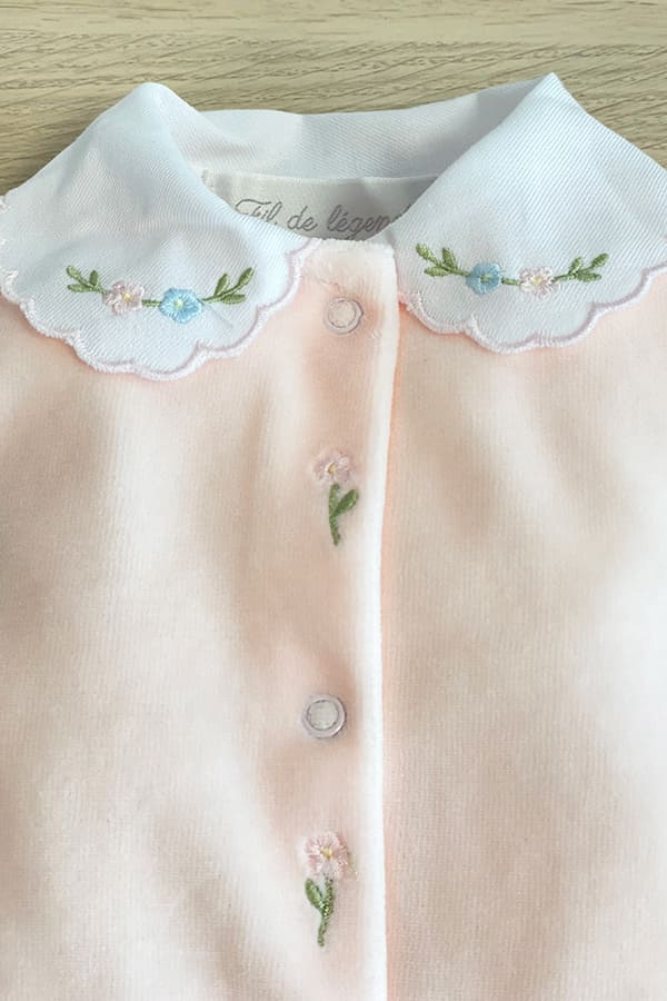 Détail du pyjama bébé fille Eva en velours de coton rose pâle, avec col blanc festonné brodé de fleurs roses et bleues et délicates broderies florales sur le devant.  Fil de Légende.