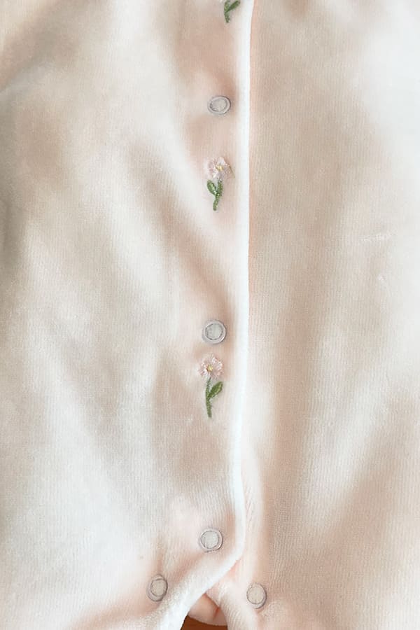 Gros plan sur les délicates fleurs roses brodées et les boutons-pression sur le devant du pyjama bébé fille Eva en velours de coton rose pâle – Fil de Légende.