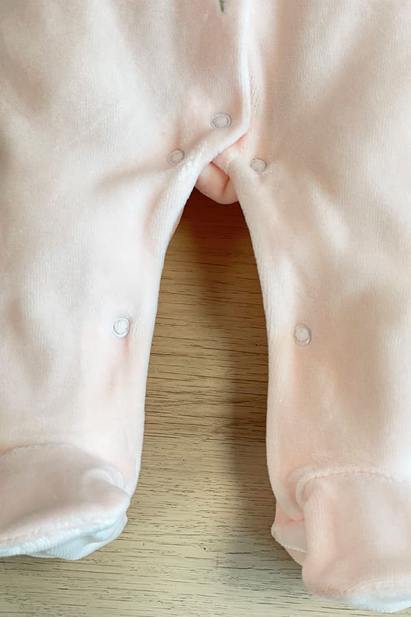 Gros plan sur le bas du pyjama bébé fille Eva en velours de coton rose pâle, montrant les pieds intégrés et l'ouverture par boutons-pression à l'entrejambe et le long des jambes, pour faciliter le change – Fil de Légende.