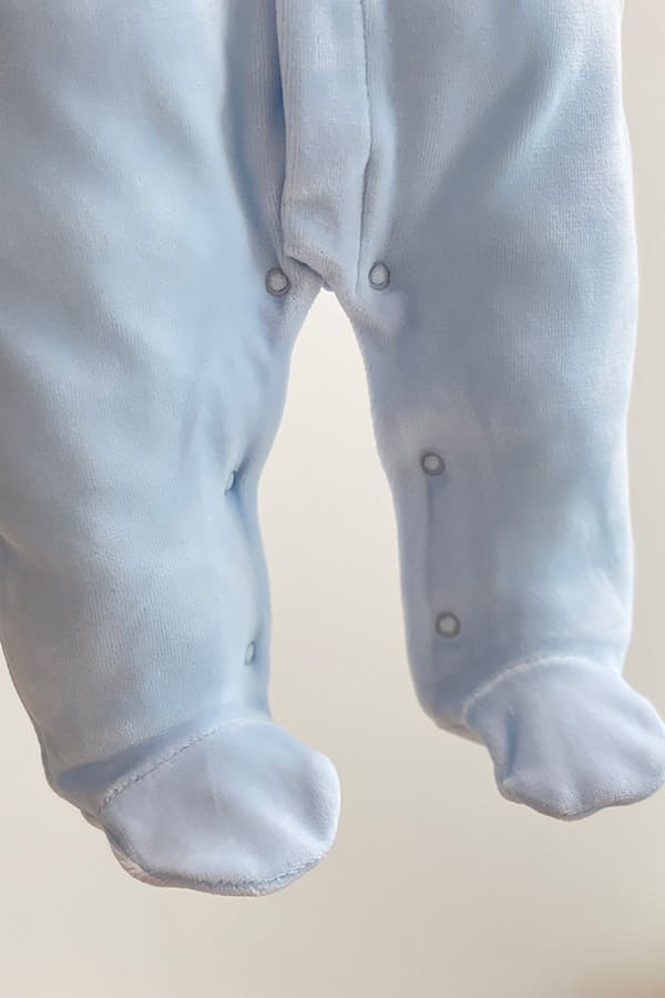 Gros plan sur le bas du pyjama bébé garçon Elio en velours de coton bleu ciel, montrant les pieds intégrés et l'ouverture par boutons-pression à l'entrejambe et le long des jambes pour faciliter le change – Fil de Légende.