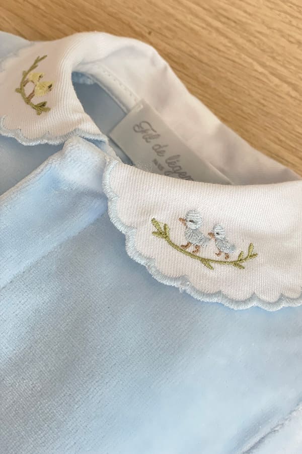 Gros plan sur le col blanc festonné du pyjama bébé garçon Elio en velours de coton bleu ciel, orné de broderies représentant de petits oiseaux bleus posés sur une branche – Fil de Légende.