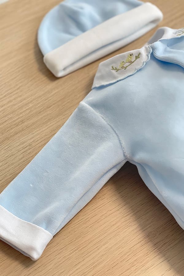 Gros plan sur la manche du pyjama bébé garçon Elio en velours de coton bleu ciel, avec revers blanc au poignet, col blanc brodé de petits oiseaux et bonnet assorti bleu ciel à revers blanc.