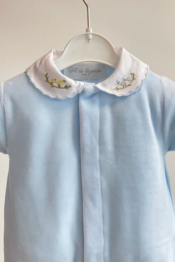 Vue rapprochée du haut du pyjama bébé garçon Elio en velours de coton bleu ciel, présenté sur cintre, avec col blanc festonné brodé de petits oiseaux jaunes et bleus et patte de boutonnage dissimulée – Fil de Légende.