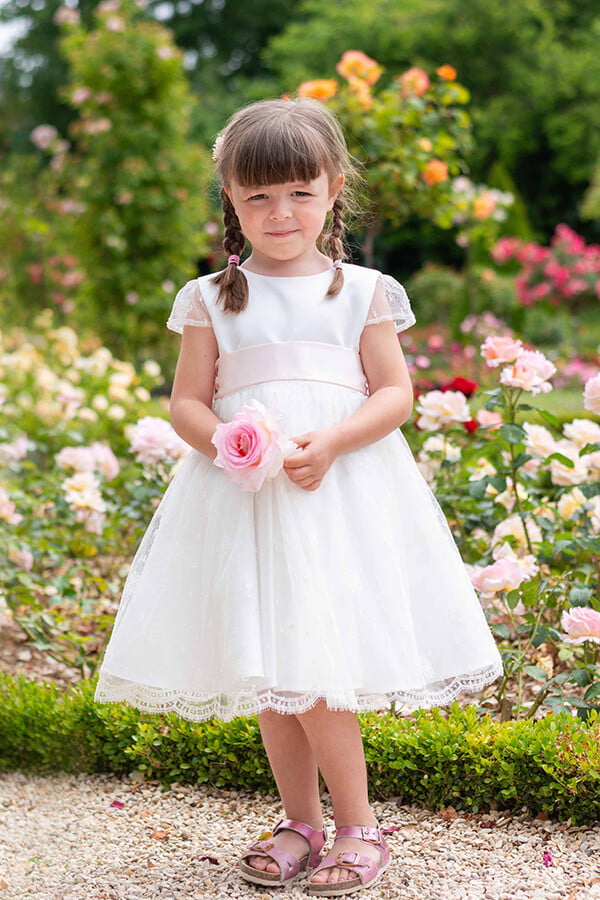 Robe de baptême ou de cérémonie pour bébé et petite fille en dentelle de Calais, doublée de satin, modèle été à manches courtes. Création Fil de Légende. Photo de robe portée par une petite fille avec une rose.