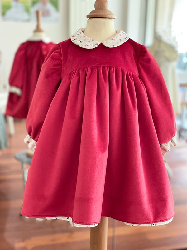 Robe de Noël pour bébé et petite fille en velours rouge avec un col aux motifs de Noël et une fronce en bas des manches. Boutique Fil de Légende à Paris, Neuilly-sur-Seine.
