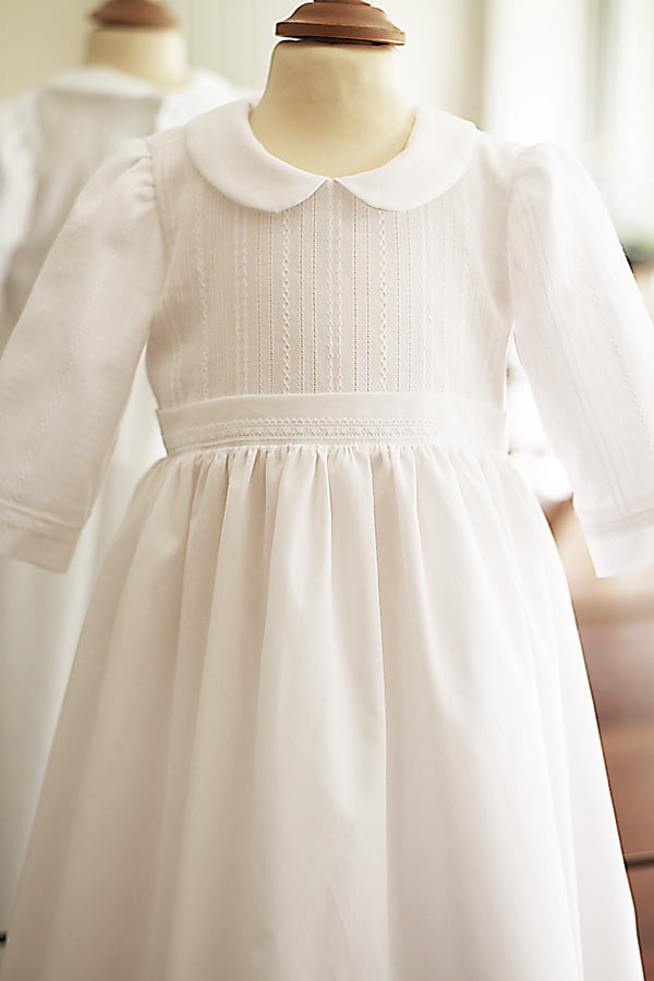 Robe traditionnelle mixte en coton blanc pour bébé fille et garçon. Corsage en coton brodé et dentelle de coton. Modèle manches longues. Création française Fil de Légende. Photo de la robe portée sur un mannequin de couture.
