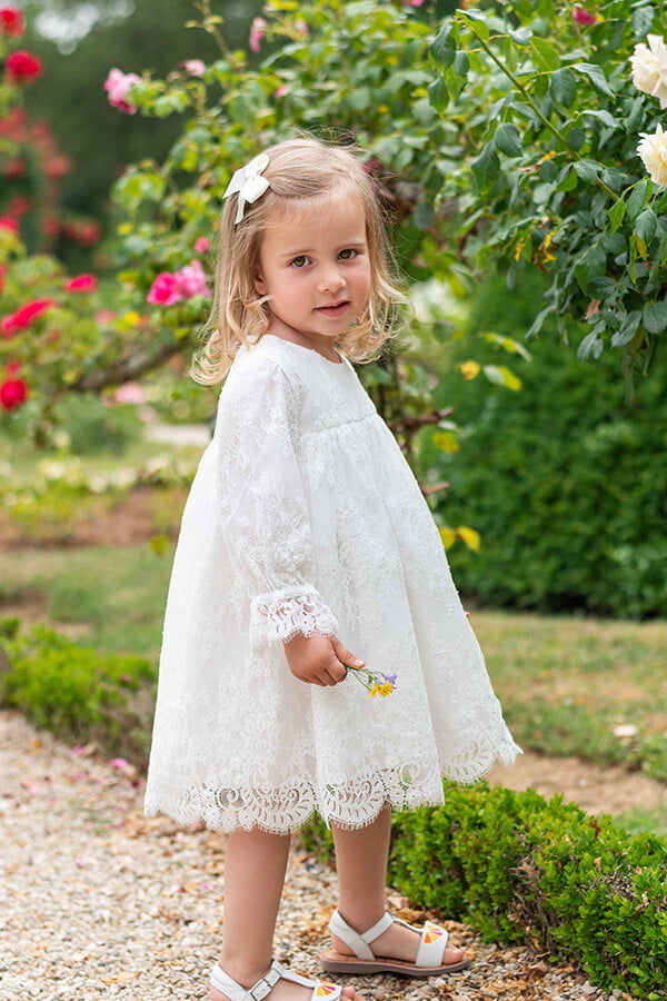 Robe de baptême ou de cérémonie pour bébé et petite fille en dentelle italienne, doublée de coton, modèle printemps à manches longues. Création Fil de Légende. Photo de la robe portée par une petite fille.