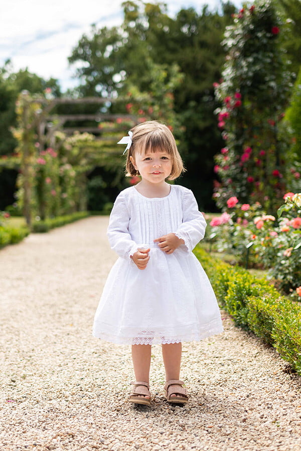 Robe de baptême et de cérémonie pour bébé fille, en broderie anglaise blanche et dentelle de Calais. Robe de baptême haut de gamme, création française Fil de Légende. Photo de la robe portée par une petite fille.