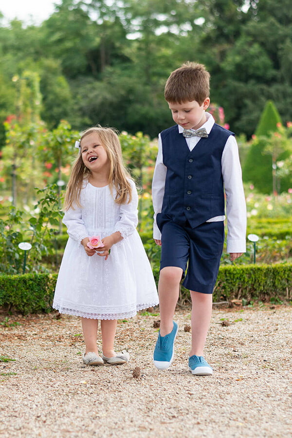 Robe de baptême et de cérémonie pour bébé fille, en broderie anglaise blanche et dentelle de Calais. Robe de baptême haut de gamme, création française Fil de Légende. Photo de la robe portée par une petite fille avec un petit garçon.