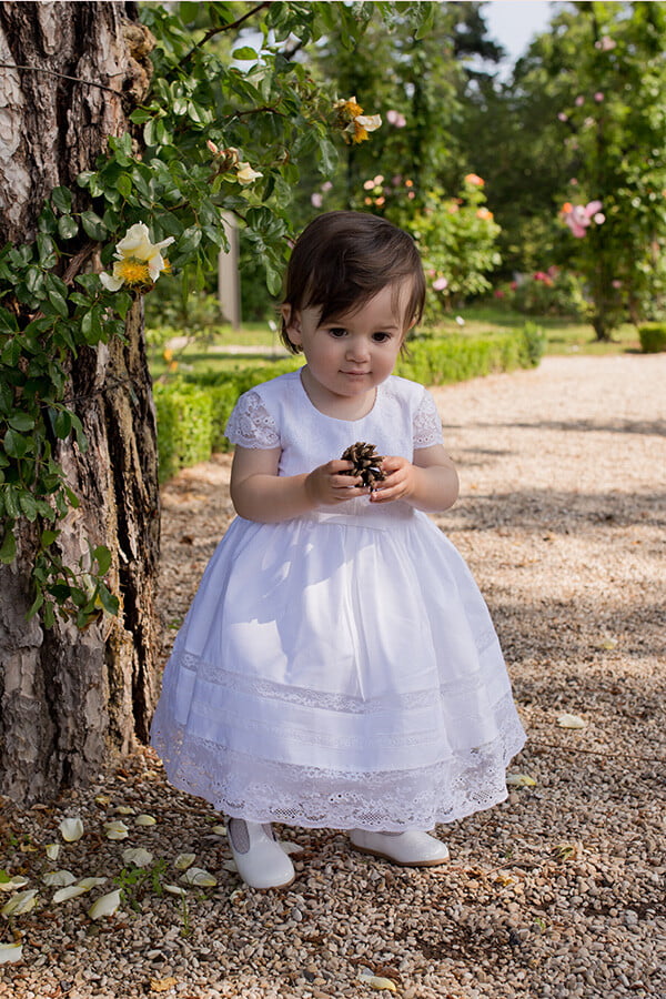 Robe de baptême pour bébé fille en coton blanc et dentelle de Calais, modèle été à manches courtes. Création française Fil de Légende. Photo de robe portée par une petite fille.