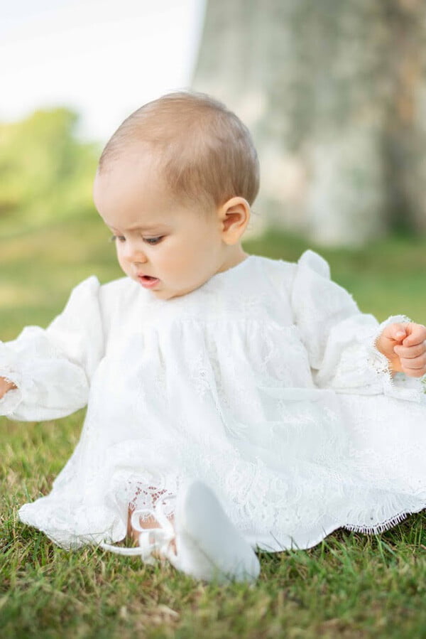 Robe de baptême ou de cérémonie pour bébé et petite fille en dentelle italienne, doublée de coton, modèle printemps à manches longues. Création Fil de Légende. Photo d'un bébé fille portant la robe.