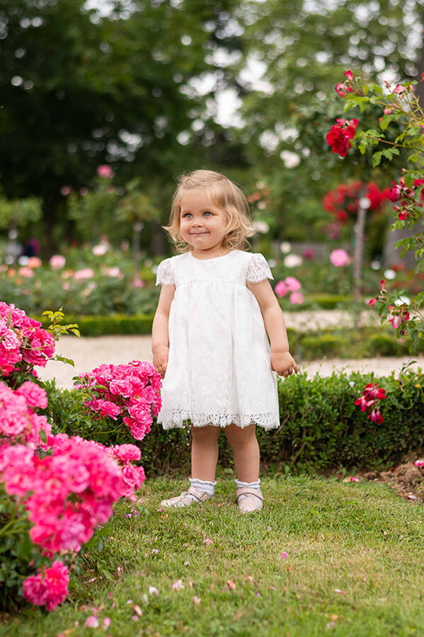 Robe de baptême ou de cérémonie pour bébé et petite fille en dentelle italienne, doublée de coton, modèle été à manches courtes. Création Fil de Légende. Photo de la robe portée par une petite fille dans un parc.