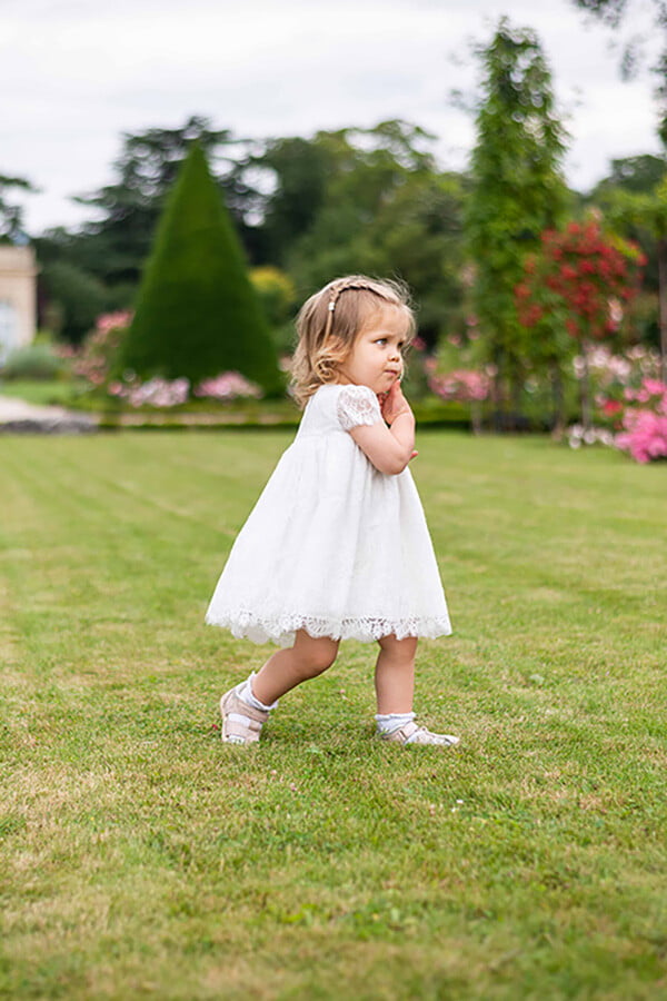 Robe de baptême ou de cérémonie pour bébé et petite fille en dentelle italienne, doublée de coton, modèle été à manches courtes. Création Fil de Légende. Photo de la robe portée par une petite fille qui marche.