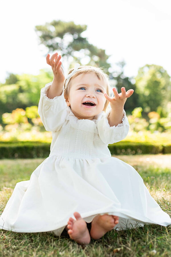 Robe de baptême fille pour l'hiver en velours blanc cassé et dentelle de Calais, doublée polaire. Création française Fil de Légende. Photo de la robe portée par une petite fille.