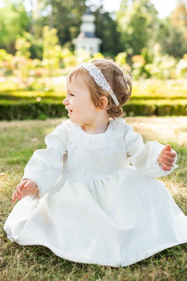 Robe de baptême fille pour l'hiver en velours blanc cassé et dentelle de Calais, doublée polaire. Création française Fil de Légende. Photo de la robe portée avec un accessoire cheveux.
