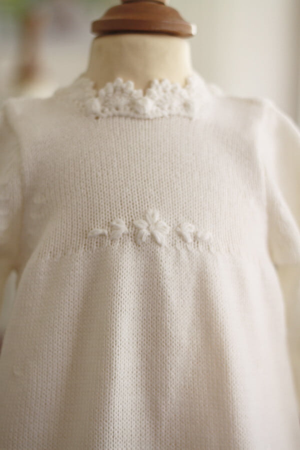 Robe baptême fille blanc cassé en maille tricotée avec bordures faites au crochet à la main. Robe en lainage. Création française Fil de Légende. Photo du motif floral sur le devant de la robe.