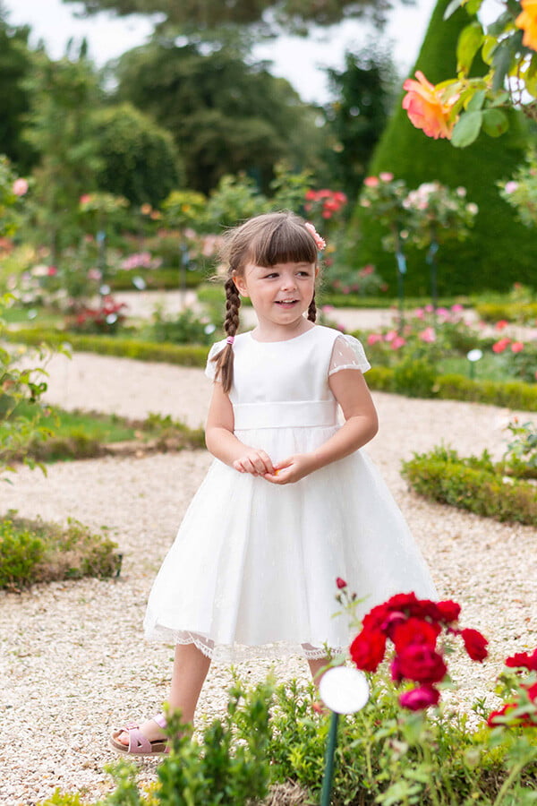 Robe de baptême ou de cérémonie pour bébé et petite fille en dentelle de Calais, doublée de satin, modèle été à manches courtes. Création Fil de Légende. Photo de robe portée par une petite fille qui marche.