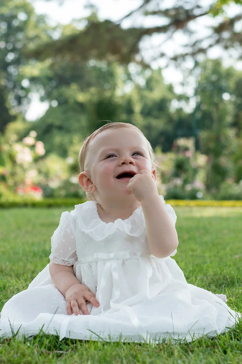 Robe de baptême bébé fille en voile plumetis doublé coton. Modèle été manches courtes. Création française Fil de Légende. Photo de robe portée par un bébé fille.