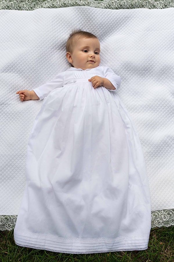 Robe de baptême traditionnelle bébé garçon Gabriel en piqué de coton blanc et dentelle de coton. Création française Fil de Légende. Photo de la robe portée par un bébé garçon allongé.