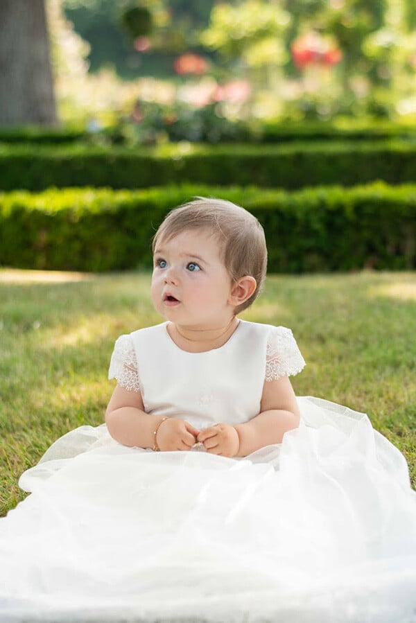 Robe baptême traditionnelle bébé fille en tulle souple brodé et dentelle doublée de satin. Modèle été manches courtes. Création française Fil de Légende.  Photo de la robe portée par une petite fille.