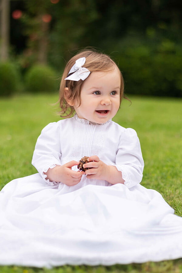 Robe baptême traditionnelle mixte pour bébé fille ou garçon en coton blanc et dentelle de Calais. Modèle manches longues. Création française Fil de Légende. Photo de la robe portée par une petite fille.