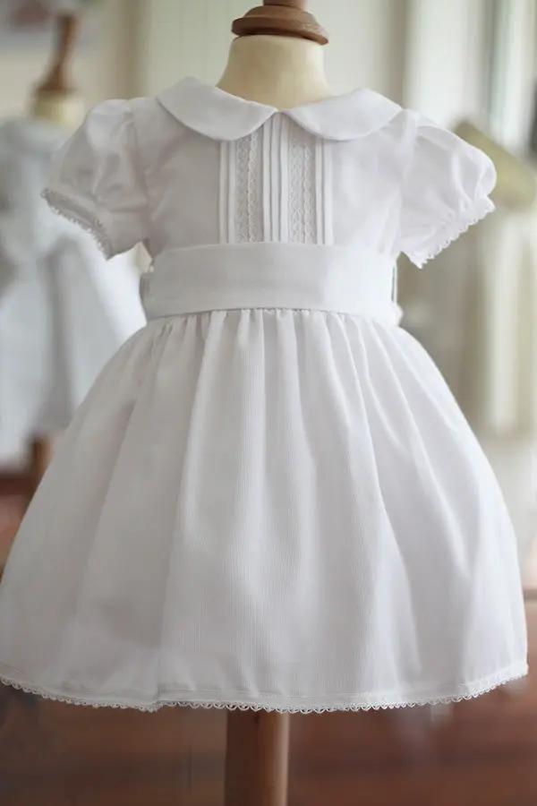 Robe de baptême et de cérémonie pour bébé et petite fille, en piqué de coton blanc et dentelle de coton. Ceinture au choix blanche ou rose. Création française Fil de Légende. Disponible en ligne ou en boutique showroom à Paris-Neuilly-sur-Seine.