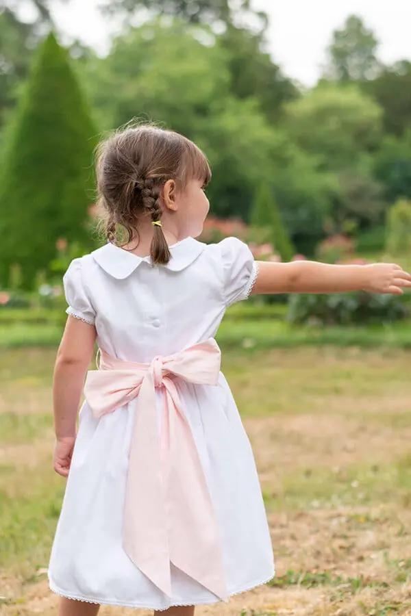 Robe de baptême et de cérémonie pour bébé et petite fille, en piqué de coton blanc et dentelle de coton. Ceinture au choix blanche ou rose. Création française Fil de Légende. Photo de la robe vue de dos.