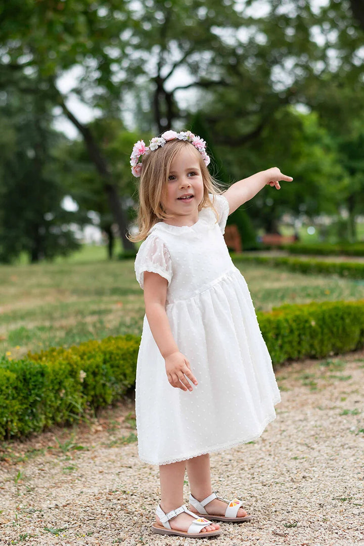 Robe de baptême bébé fille en voile plumetis doublé coton. Modèle été manches courtes. Création française Fil de Légende. Photo de robe portée par une petite fille dans un jardin.
