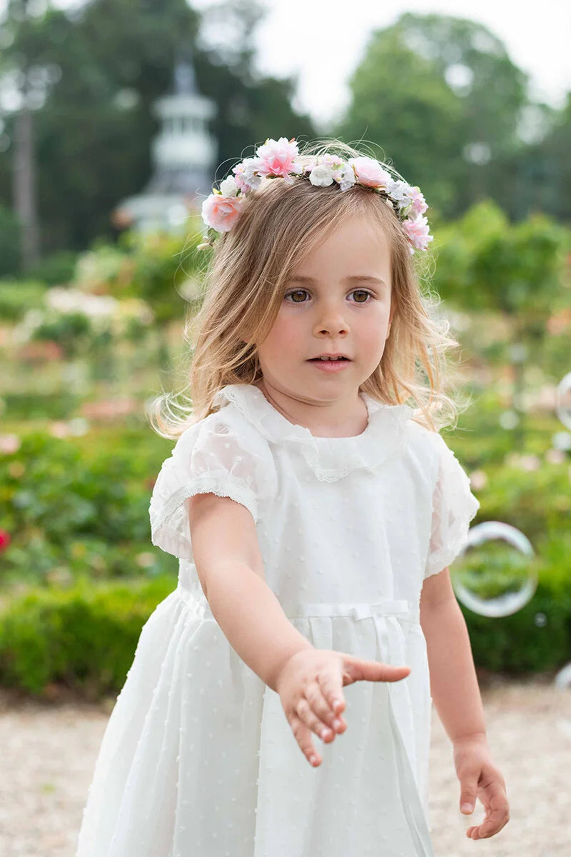 Robe de baptême bébé fille en voile plumetis doublé coton. Modèle été manches courtes. Création française Fil de Légende. Photo de robe portée avec une couronne de fleurs.