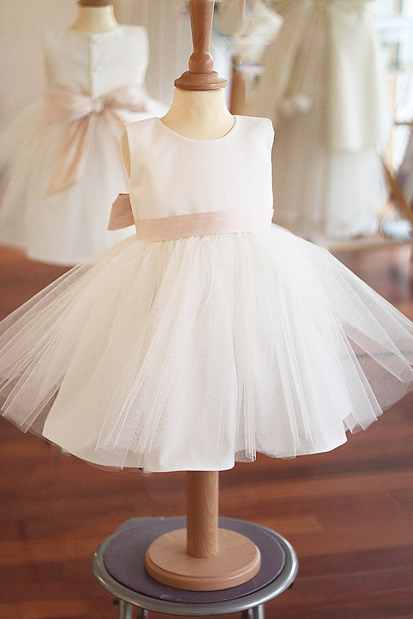 Robe de baptême ou de cérémonie pour bébé fille en coton blanc cassé avec une jupe en tulle et une ceinture rose poudré. Boutique Fil de Légende à Paris, Neuilly-sur-Seine.