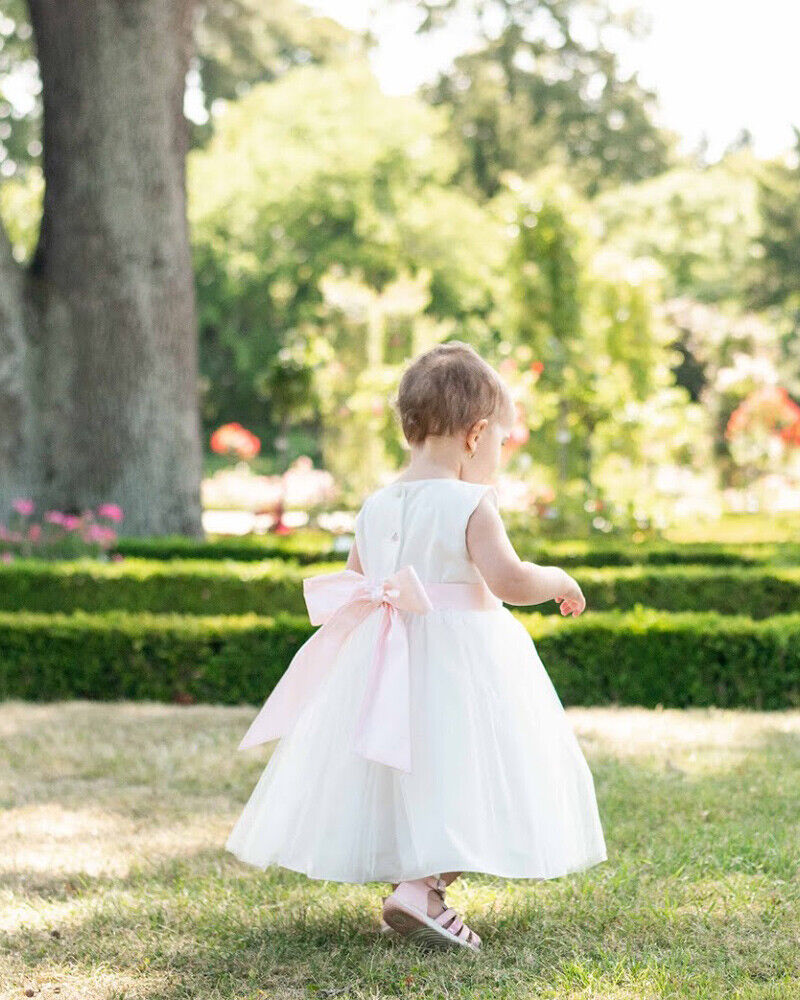 Robe de baptême ou de cérémonie pour bébé fille en coton blanc cassé avec une jupe en tulle et une ceinture rose poudré. Robe vue de dos.