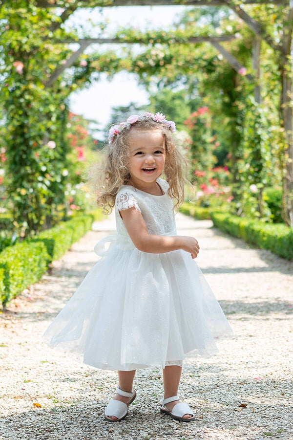 Robe de baptême et de cérémonie pour bébé fille, corsage en dentelle italienne blanc cassé, jupe en tulle pailleté, ceinture en soie. Robe de baptême haut de gamme, création française Fil de Légende. Photo de la robe portée par une petite fille qui marche.