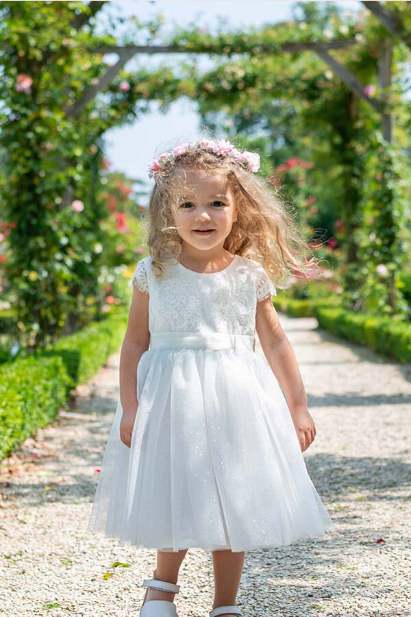 Robe de baptême et de cérémonie pour bébé fille, corsage en dentelle italienne blanc cassé, jupe en tulle pailleté, ceinture en soie. Robe de baptême haut de gamme, création française Fil de Légende. Photo de la robe portée par une petite fille.