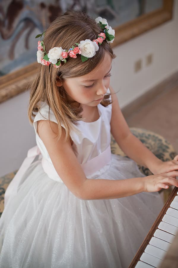 Robe cérémonie fille Lucie en taffetas et tulle pailleté blanc, ceinture rose. Photo de la robe portée par une petite fille assise.