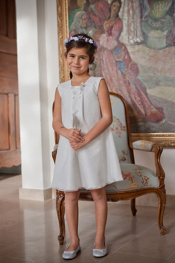 Robe de cérémonie fille trapèze en Shantung et tulle pailleté. Photo de la robe portée par une petite fille debout.