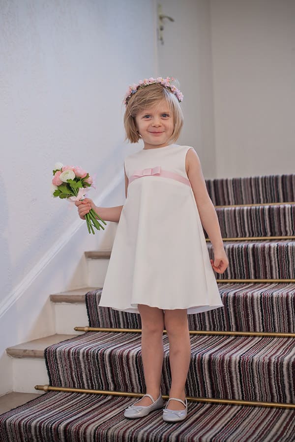 Robe trapèze cérémonie fille en coton blanc cassé et ruban rose. Photo de la robe vue de trois quart.