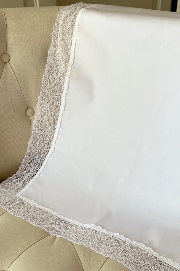 Serviette de baptême en coton blanc bordée d'un large galon de dentelle italienne blanche. Vue de côté.