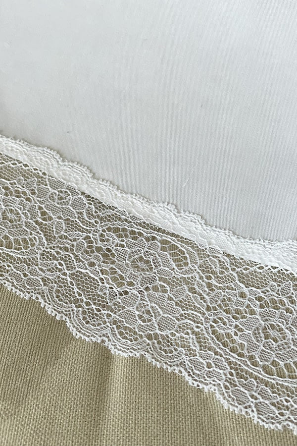 Serviette de baptême en coton blanc bordée d'un large galon de dentelle italienne blanche. Gros plan sur bordure.