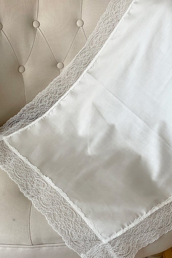 Serviette de baptême en coton blanc bordée d'un large galon de dentelle italienne blanche. Vue de côté gros plan.