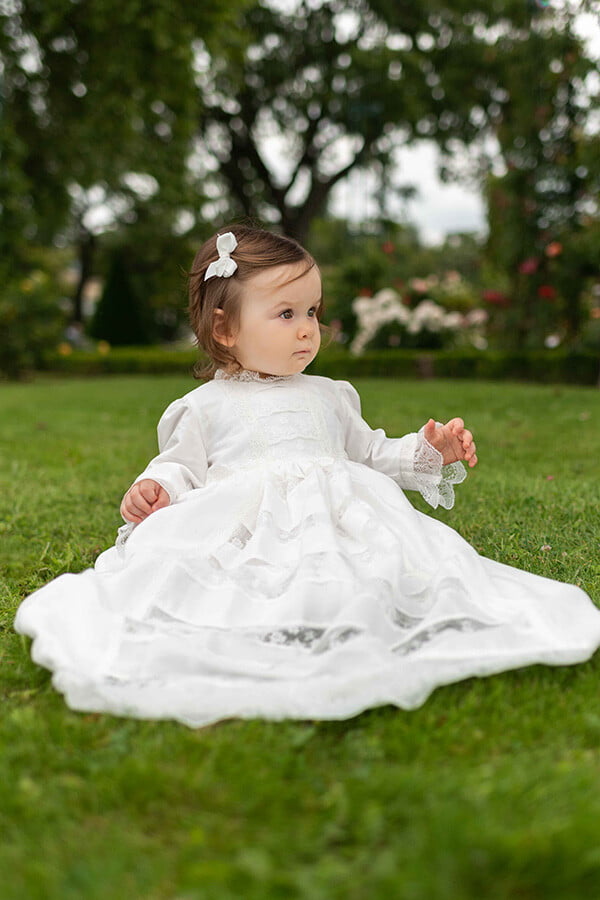 Robe de baptême traditionnelle bébé en coton et dentelle de Calais blanc cassé. Modèle manches longues. Création française Fil de Légende. Photo de la robe portée par une petite fille.